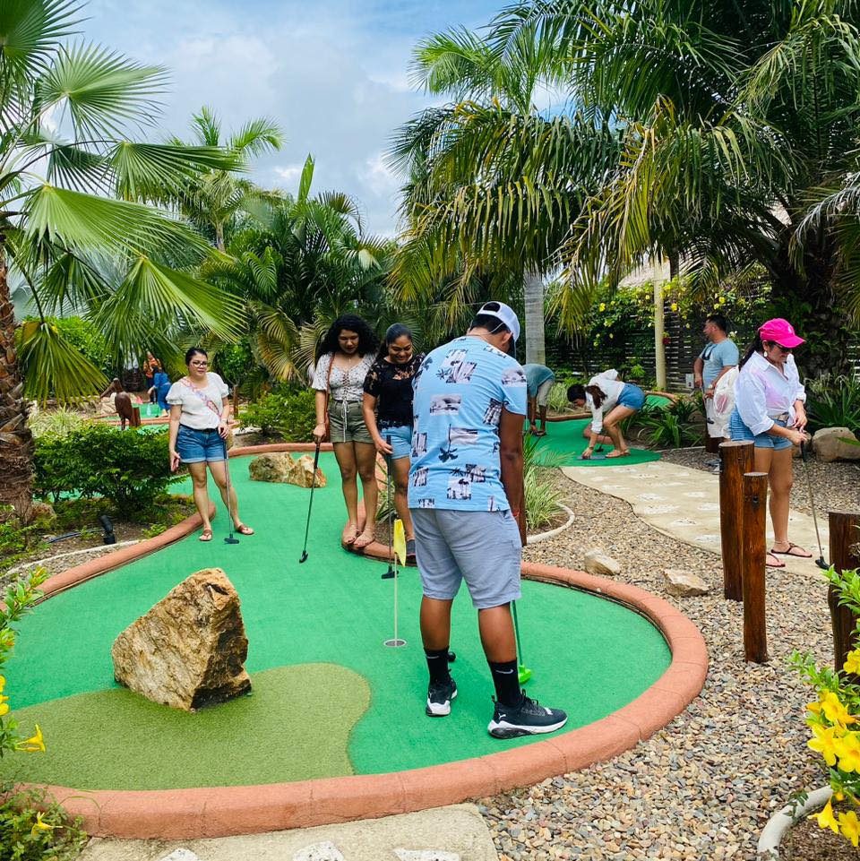 Guests play mini-golf at Inky’s Belize surrounded by palm trees and tropical landscaping, highlighting a nearby recreation option within easy reach of Marazul Belize.
