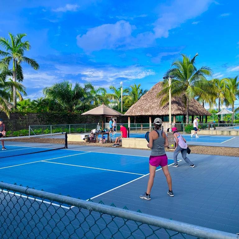 Guests play pickleball on outdoor courts at Inky’s Belize, surrounded by palm trees and tropical landscaping, highlighting a nearby recreation option close to Marazul Belize.